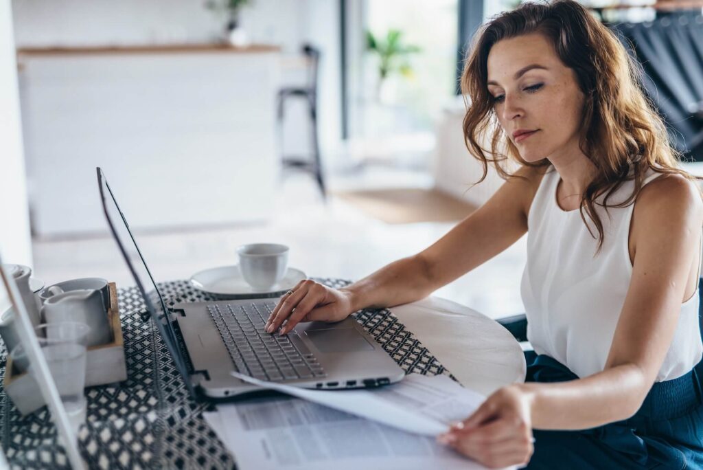 A woman looking at some papers while working on a laptop