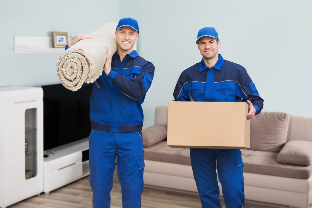 Two international movers, one holding a package, another holding a rolled carpet