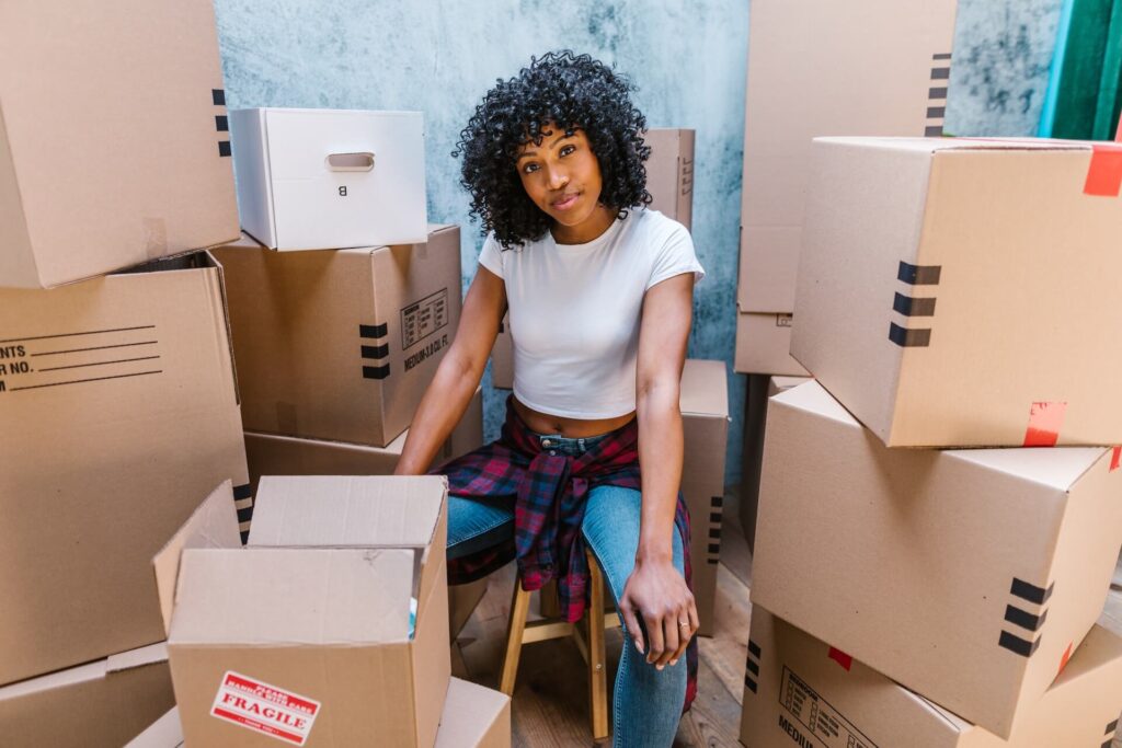 Young woman sitting on a stool, surrounded by boxes before moving overseas