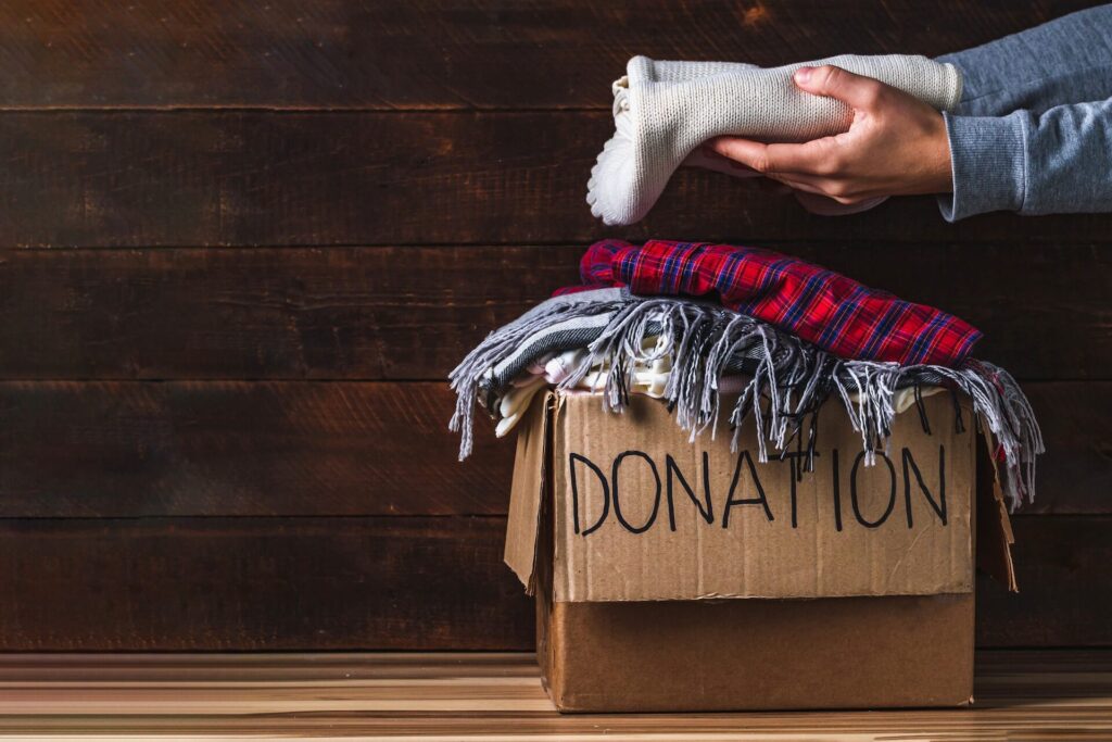 Person putting clothing into a box labeled for donation before moving overseas