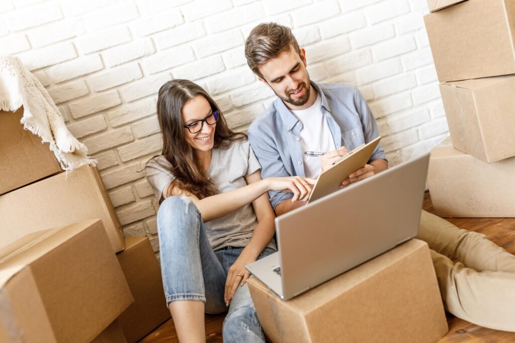 A couple booking an international mover on a laptop while surrounded by boxes