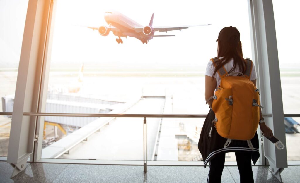 Woman with a backpack standing at the airport, watching an airplane