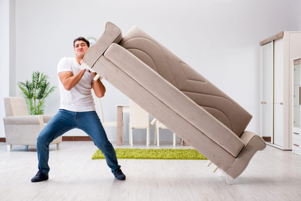 A man trying to move a gray sofa